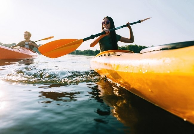 Zwei Paddler gleiten im Kajak über ruhiges Wasser im Everglades NP, während Sonnenlicht die orangefarbenen Boote und das Paddel beleuchtet.