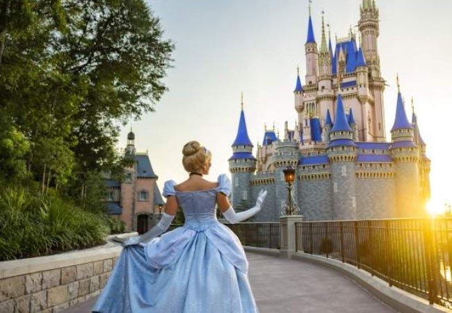 Eine Frau im blauen Ballkleid steht vor dem märchenhaften Cinderella Castle im Magic Kingdom, während die Sonne warm über Orlando leuchtet.