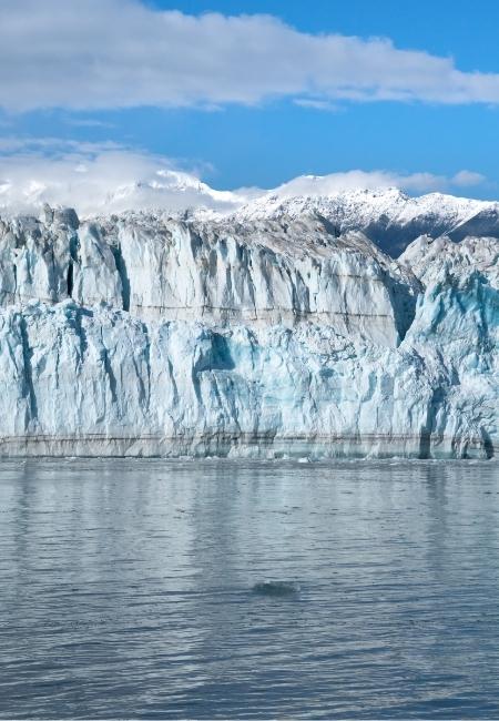 Der Hubbard Glacier zeigt eine gewaltige blaue Eiswand vor verschneiten Bergen und ruhigem Wasser in Alaska.