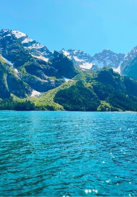 Türkisblaues Wasser vor einer wilden Küste mit schneebedeckten Bergen am Prince William Sound in Alaska.