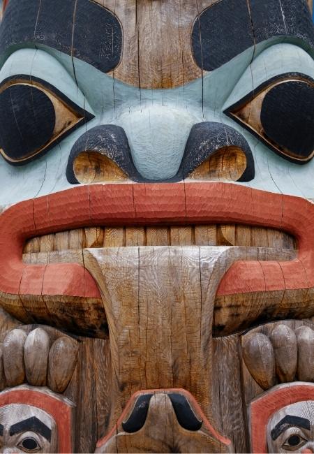 Ein bemalter Totempfahl aus Holz zeigt ein markantes geschnitztes Gesicht mit roten Lippen und blauen Konturen.