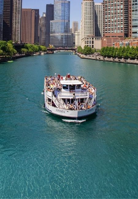 Ein Ausflugsboot fährt über den Chicago River, während die Wolkenkratzer der Innenstadt dicht am Ufer aufragen.