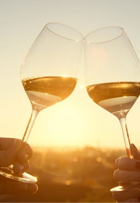 Zwei Weingläser stoßen im warmen Sonnenuntergang an, während das Licht die Szenerie in Gold taucht.