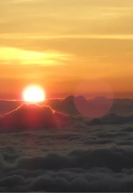 Die Sonne steigt über dem Haleakalā auf und taucht den Himmel über einer dichten Wolkendecke in warmes Orange.