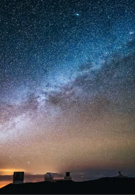 Über den dunklen Hügeln von Mauna Kea spannt sich ein dichter Sternenhimmel mit der Milchstraße über Hawaii.