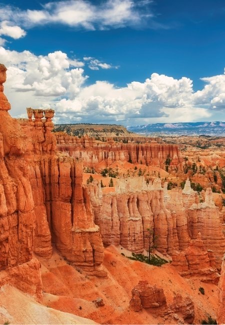 Rote Felsnadeln und steile Schluchten im Bryce Canyon leuchten unter tiefblauem Himmel mit markanten weißen Wolken und weiter Felslandschaft.
