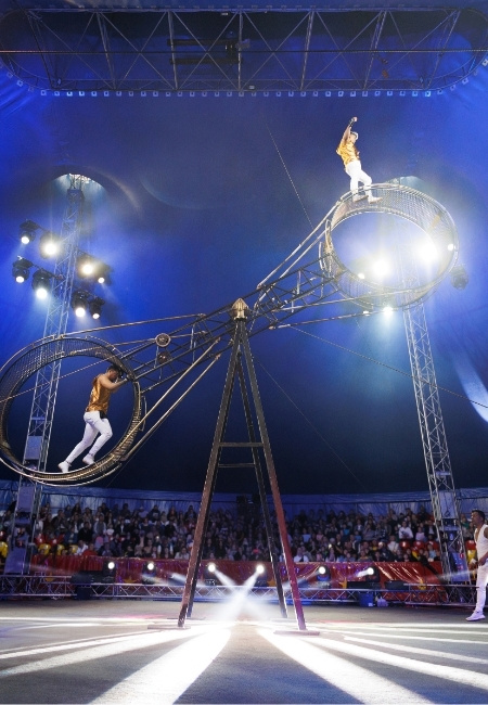 Unter blauem Licht balancieren zwei Akrobaten im Cirque du Soleil auf großen Metallreifen vor dicht besetztem Publikum in Las Vegas.