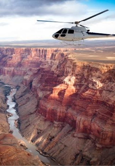 Ein weißer Helikopter fliegt über dem Grand Canyon mit tiefen Felsklippen und dem Flussbett im Tal in der weiten Wüstenlandschaft.