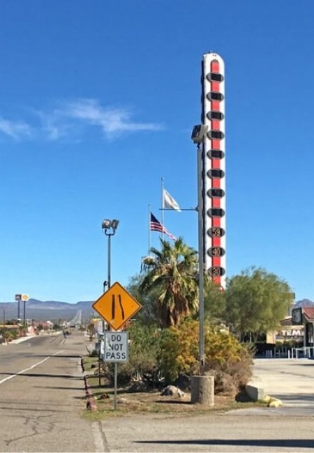 Am Straßenrand in der Wüste von Las Vegas ragt das höchste Thermometer der Welt neben Palmen, Schildern und blauem Himmel deutlich auf.