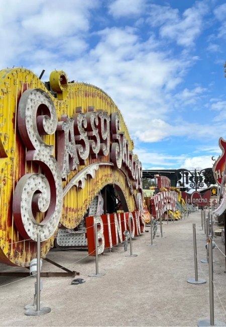Historische Leuchtreklamen im Neon Museum Las Vegas säumen einen Weg unter blauem Himmel, darunter das große „Blenko“ und weitere Vintage-Schilder.
