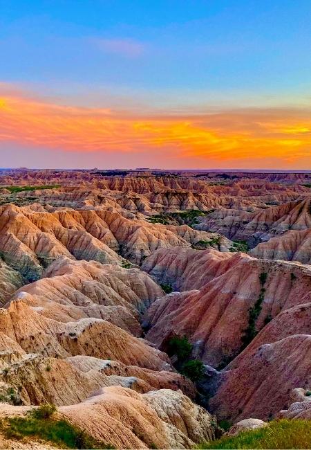 Im Badlands Nationalpark leuchten zerklüftete, rötliche Felsrippen unter einem intensiven Sonnenuntergangshimmel.