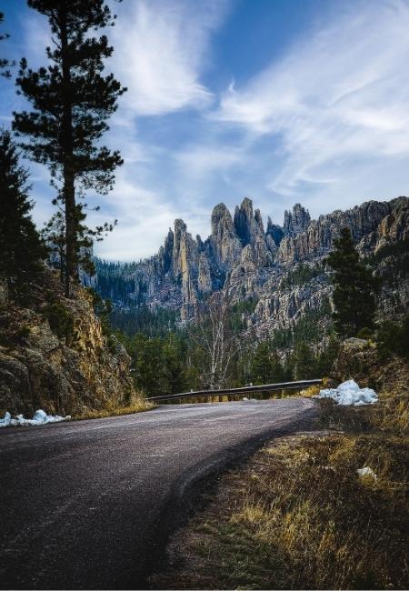 Eine kurvige Straße führt durch Custer State Park zu den Felsnadeln der Needles Highway, flankiert von Schnee und Kiefern.