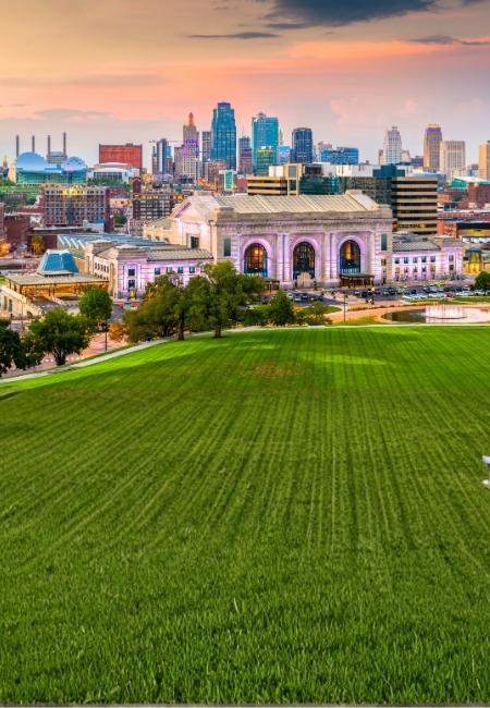 Die Skyline von Kansas City erhebt sich hinter der Union Station, davor liegt eine weite grüne Wiese im Abendlicht.