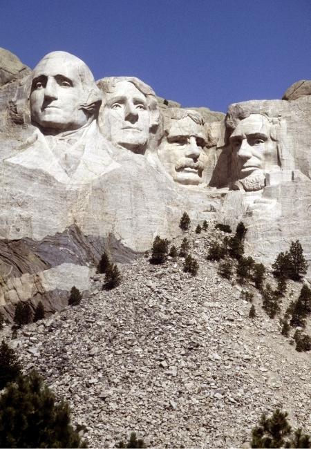 Die vier Präsidentenköpfe von Mount Rushmore ragen über hellem Fels unter einem klaren blauen Himmel auf.
