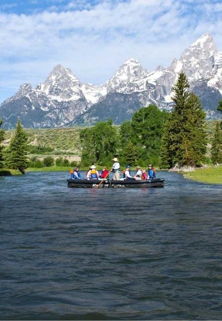 Auf dem Snake River fährt ein Floß mit mehreren Ausflüglern vor schneebedeckten Berggipfeln dahin.