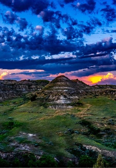 Zerklüftete Hügel im Theodore Roosevelt Nationalpark liegen unter tiefblauem Himmel und orangefarbenem Abendlicht.