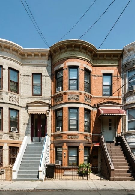 Dreistöckige Backstein-Reihenhäuser in Ridgewood, Queens, mit Treppenaufgängen und typischen Fassaden unter freiem Himmel.