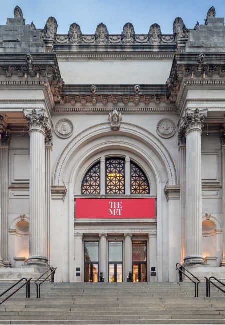 Vor dem Metropolitan Museum of Art in New York führt eine breite Treppe zum Eingang mit rotem The-Met-Schild.
