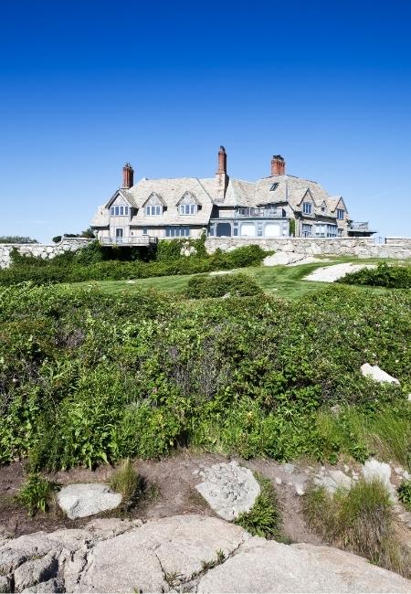 Ein historisches Steinhaus von Newport Mansions steht auf einer grünen Klippe unter klarem, blauem Himmel.