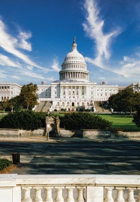 Das US-Kapitol in Washington DC erhebt sich mit weißer Kuppel vor einem tiefblauen Himmel und hellen Schleierwolken.