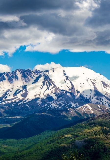 Der schneebedeckte Mount St. Helens ragt über grüne Waldhänge unter dramatischen Wolken im Pacific Northwest.