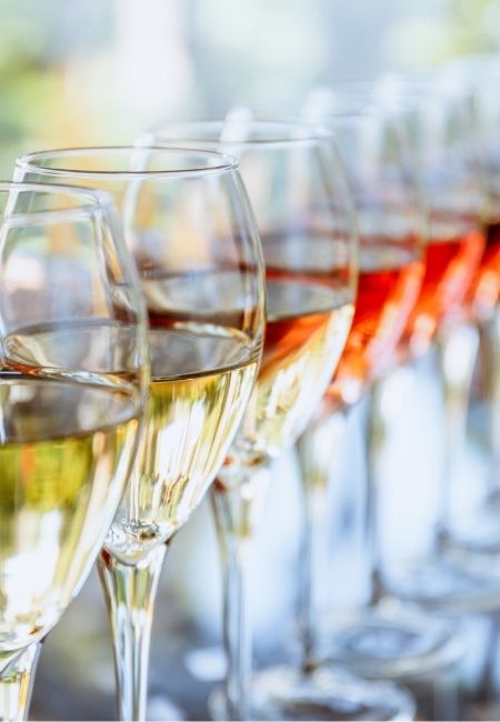 Mehrere elegante Weingläser stehen in einer Reihe und sind mit hellem und roséfarbenem Wein gefüllt.
