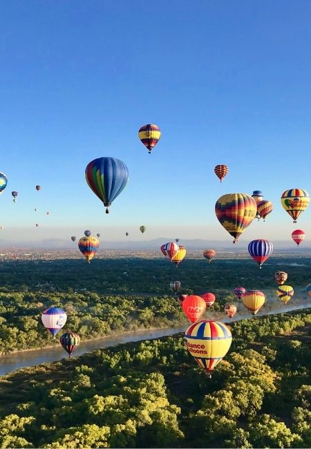 Über Albuquerque schweben viele bunte Heißluftballons über grünem Flussland und weiter Landschaft unter klarem Himmel.