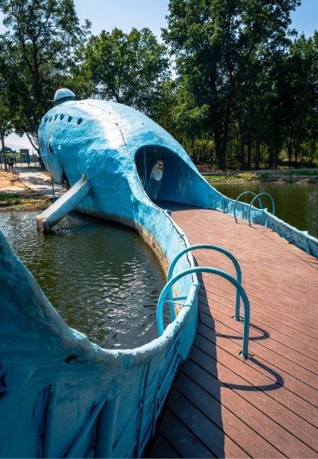 Im Wasser steht die Blue Whale of Catoosa, deren blauer Körper einen geschwungenen Steg über den Teich bildet.