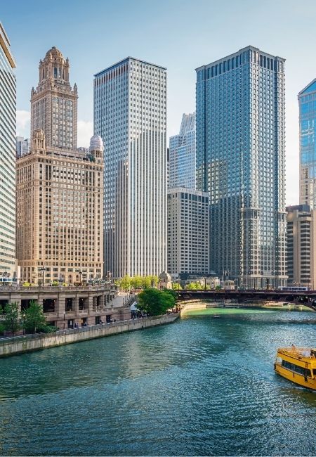 Am Chicago River ragen Wolkenkratzer in die Höhe, während ein gelbes Ausflugsboot auf dem Wasser vorbeifährt.