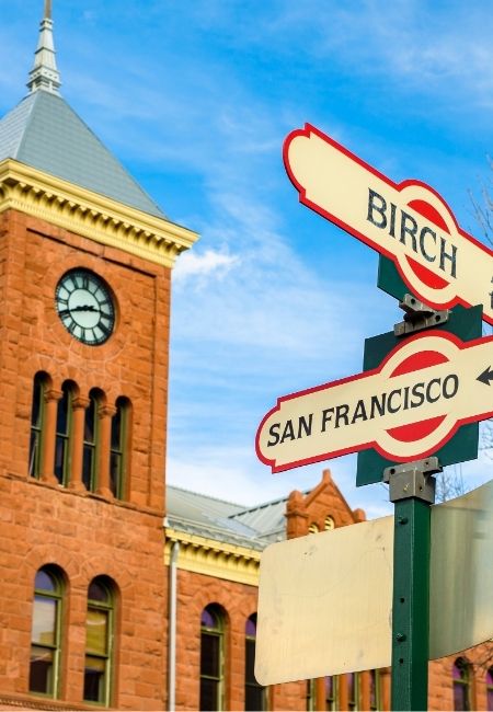 In Flagstaff zeigen Route-66-Schilder Richtung San Francisco und Birch vor einem roten Backsteingebäude mit Uhrturm.