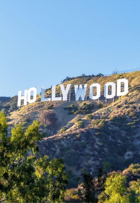 Das Hollywood Sign steht weiß leuchtend auf dem Hügel über Los Angeles unter klarem blauem Himmel.