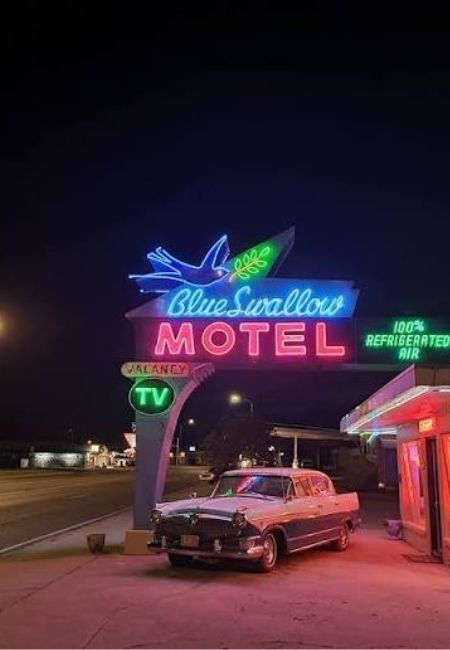 Vor dem Blue Swallow Motel in Tucumcari leuchtet ein Neon-Schild, daneben steht ein klassischer Oldtimer an der Straße.