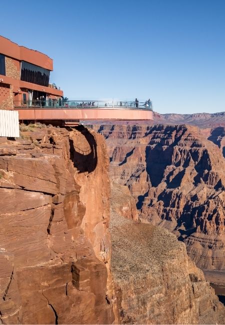 Eine Aussichtsplattform ragt über die steilen Felsen des Grand Canyon, während Besucher auf dem Glasgeländer stehen.