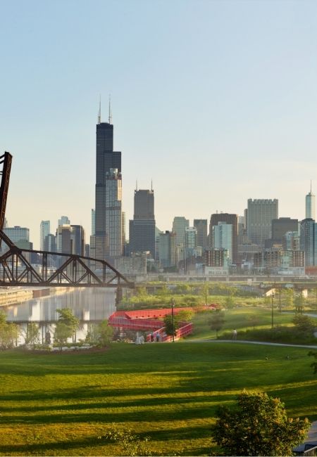 Die Skyline von Chicago mit Willis Tower, Brücke und grünem Park am Ufer bei hellem Abendlicht.