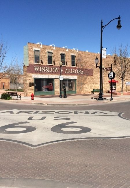 Vor einem Backsteingebäude in Winslow, Arizona ist das große Bodenmotiv „Arizona U.S. 66“ unter blauem Himmel zu sehen.