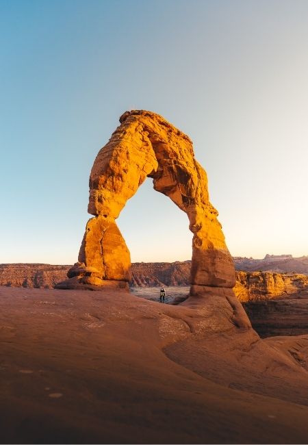 Der Delicate Arch aus rotem Sandstein leuchtet im Abendlicht über der Wüstenlandschaft des Arches National Park.