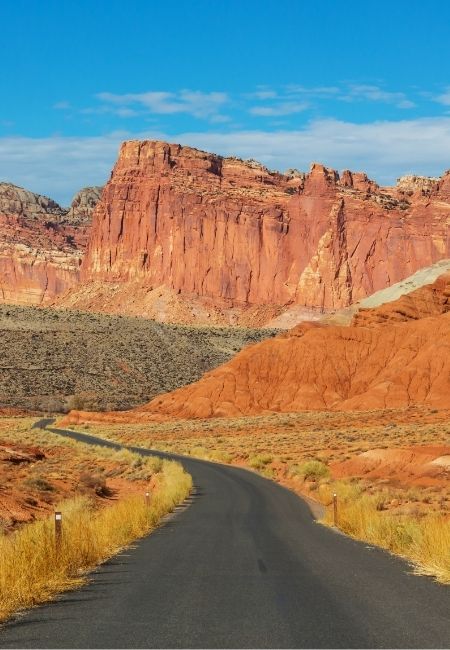 Eine asphaltierte Straße führt durch die rote Felslandschaft im Capitol Reef mit hohen Klippen und blauem Himmel.