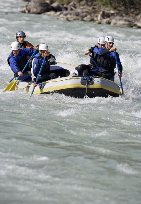 Vier Paddler mit Helmen steuern ein gelb-schwarzes Schlauchboot durch wilde Stromschnellen auf dem Colorado River.
