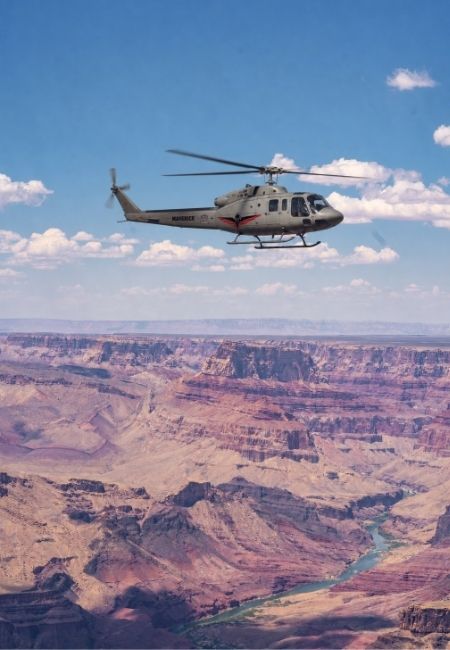 Ein Hubschrauber fliegt über den Grand Canyon vor weitem Himmel und rotbraunen Felswänden.