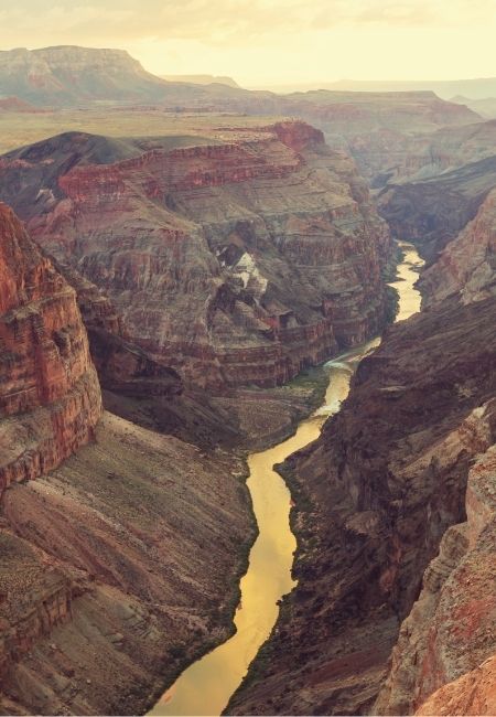 Der Colorado River schlängelt sich durch den Grand Canyon zwischen hohen roten Felswänden im warmen Abendlicht.