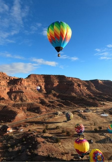 Mehrere farbige Heißluftballons schweben über den roten Felsformationen bei Kanab unter klarem blauem Himmel.
