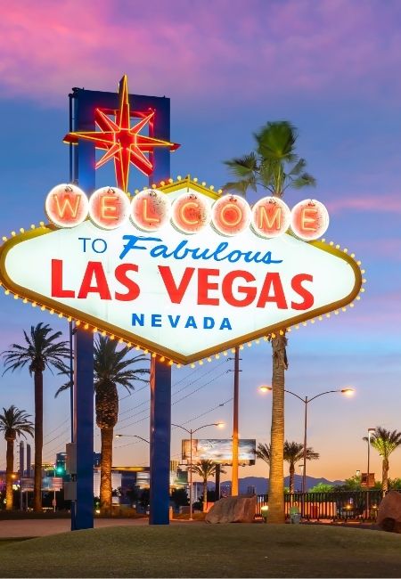 Das leuchtende Welcome-Schild in Las Vegas steht vor Palmen und einem violett-rosa Abendhimmel in Nevada.