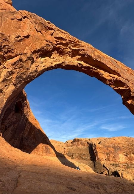 Ein natürlicher Felsbogen aus rotem Sandstein spannt sich über eine weite Wüstenlandschaft unter blauem Himmel bei Moab.