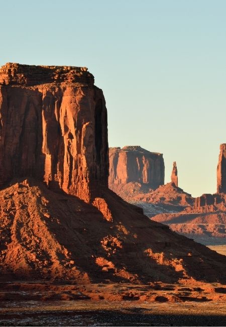 Die roten Tafelberge von Monument Valley ragen im warmen Abendlicht vor einem klaren Himmel auf.