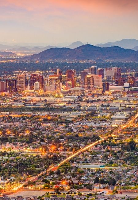 Über Phoenix leuchten Hochhäuser und Straßen bei Abenddämmerung, während die Berge von Arizona den Horizont rahmen.