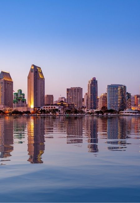 Die Skyline von San Diego leuchtet bei Abenddämmerung über ruhigem Wasser mit klaren Spiegelungen der Hochhäuser.