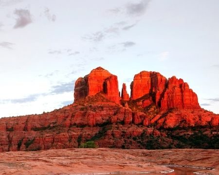 Die roten Sandsteinfelsen von Sedona spiegeln sich in einem flachen Wasserbecken vor karger Wüstenlandschaft.