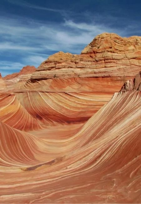 Die geschwungenen, rot-ockerfarbenen Sandsteinwellen von The Wave unter einem blauen Himmel im Südwesten der USA.