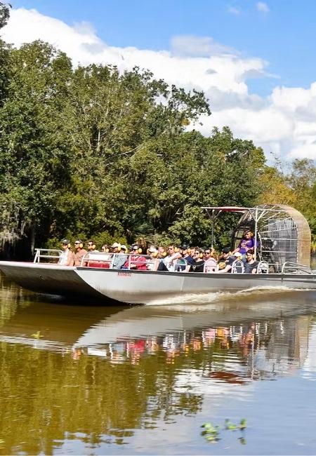 Ein weißes Airboat mit mehreren Passagieren fährt durch den Honey Island Swamp in den Südstaaten unter blauem Himmel.