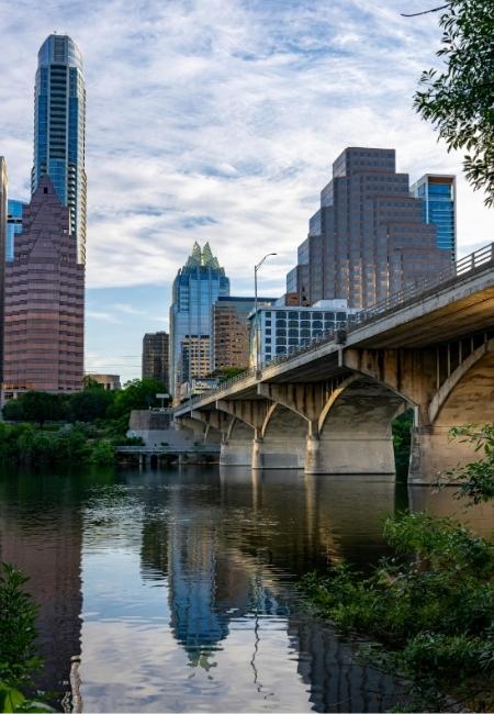 Die Skyline von Austin, Texas erhebt sich am Flussufer, während eine Brücke über dem ruhigen Wasser verläuft.